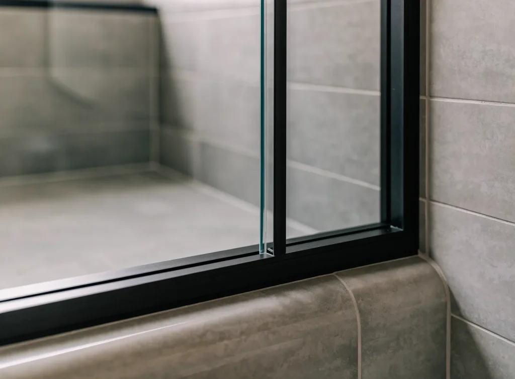 Framed glass shower screen with a slim black aluminium frame on a tiled hob